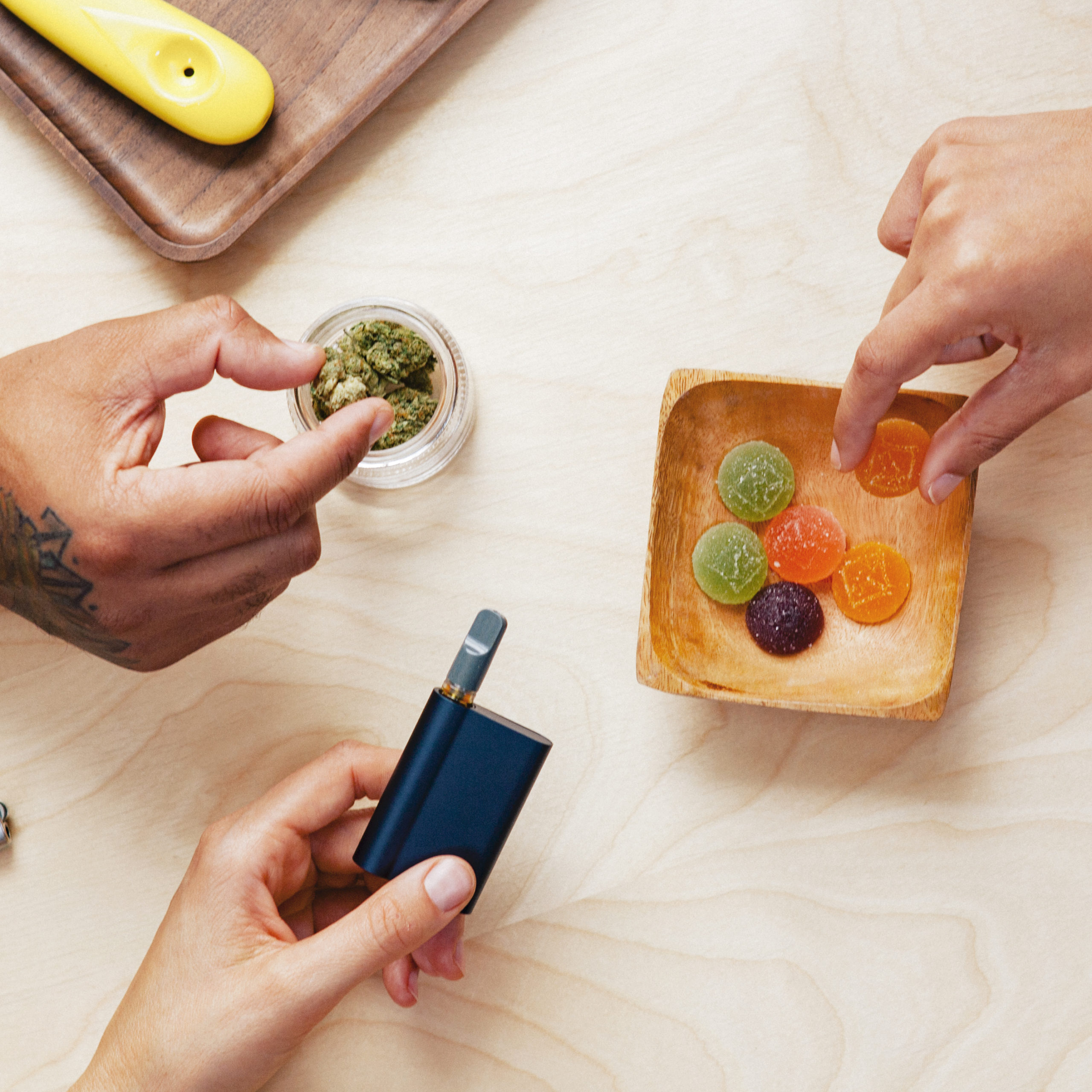 Hands holding vape pen, gummies and cannabis flower